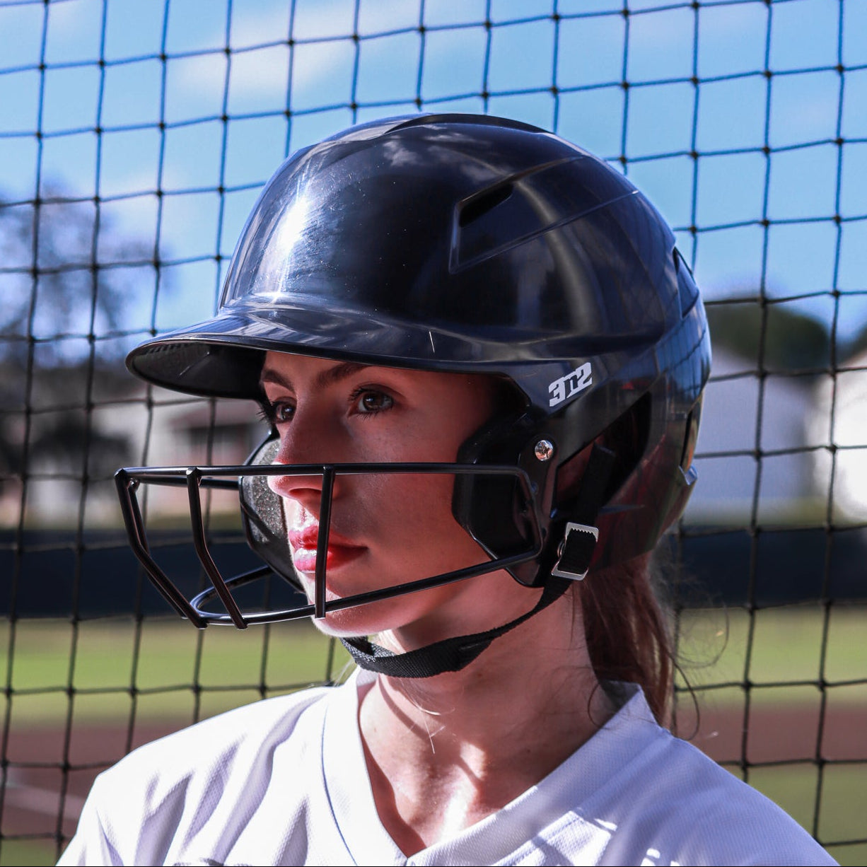 Person wearing a black helmet and white jersey with 'St. Louis' text, standing in front of a netted background.